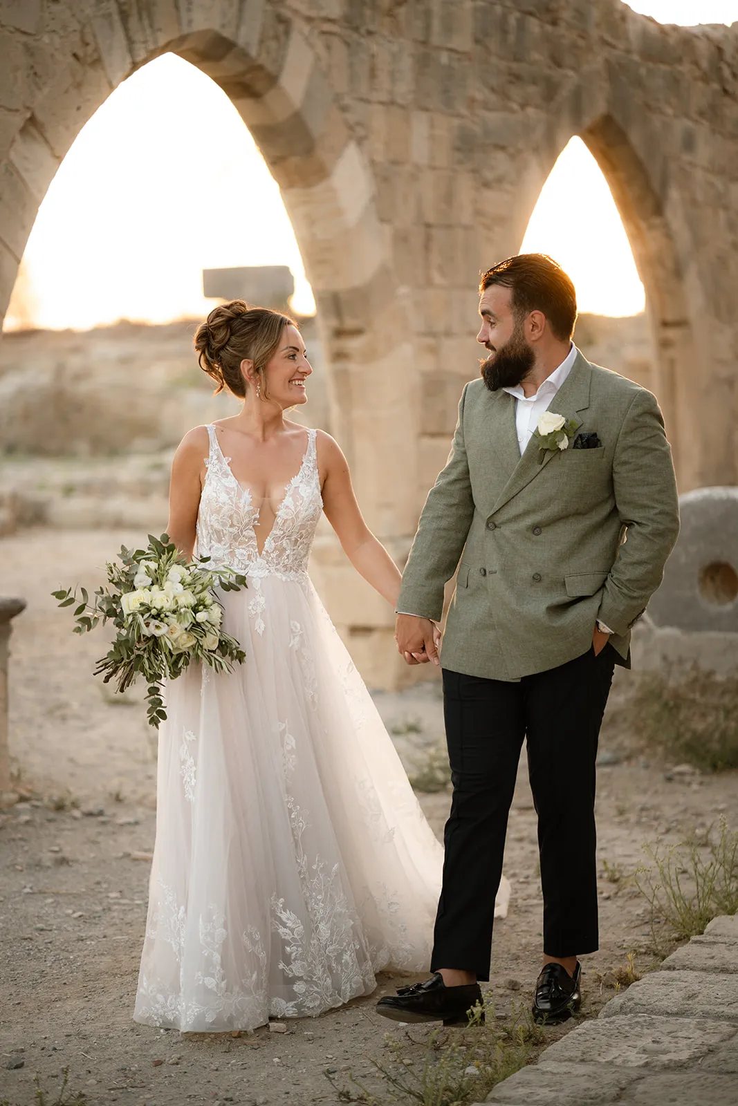 Bride and groom walking beneath stone arches at a Cyprus wedding