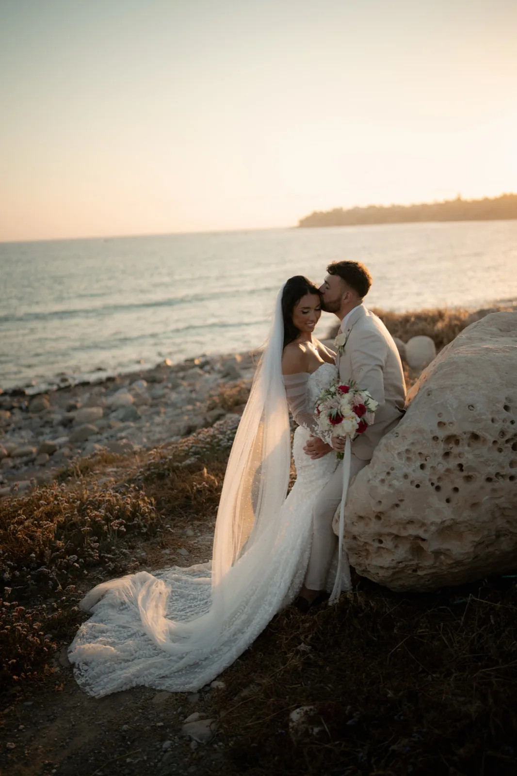 Bethanie and Jamie on the beach at sunset with the veil flowing in the sea breeze at Coral Residences, Paphos, Cyprus.