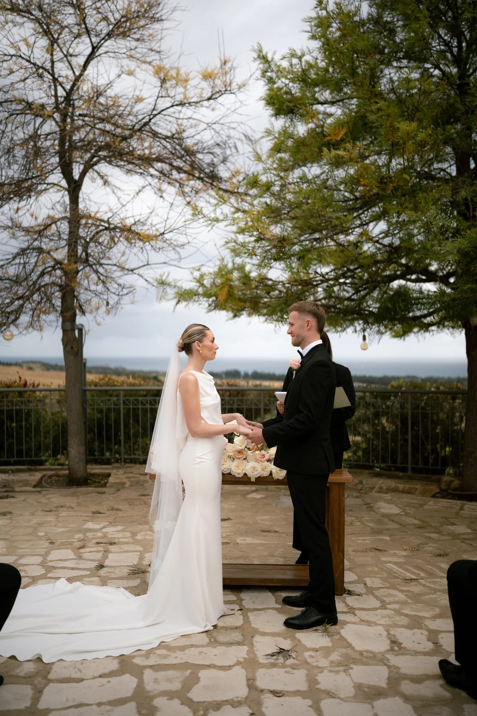 Daniel and Bailey holding hands during their vows at Liopetro, with the Paphos countryside behind them.