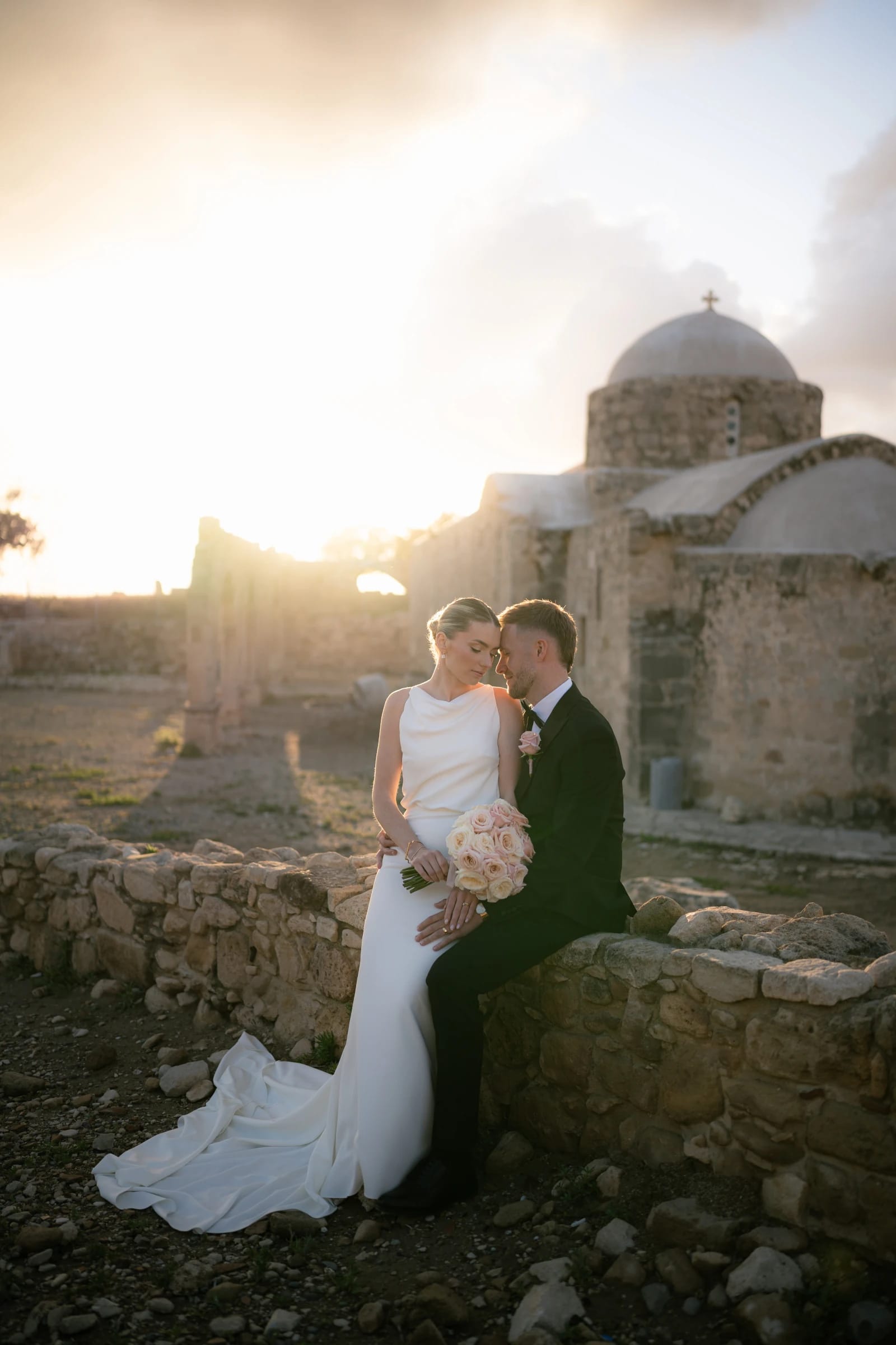 Daniel and Bailey sitting on a stone wall in front of the chapel beside Liopetro at sunset, Kouklia, Paphos.