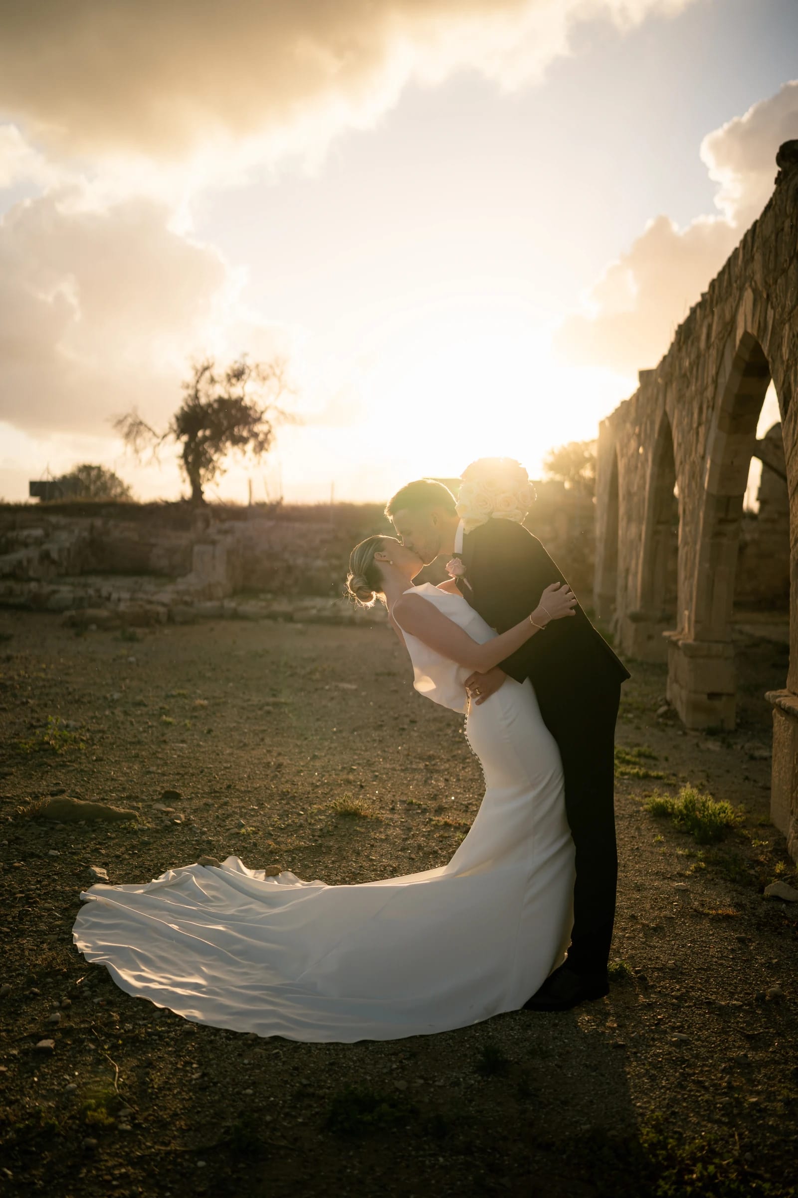 Groom dipping bride for a kiss at sunset by stone ruins at a Cyprus wedding