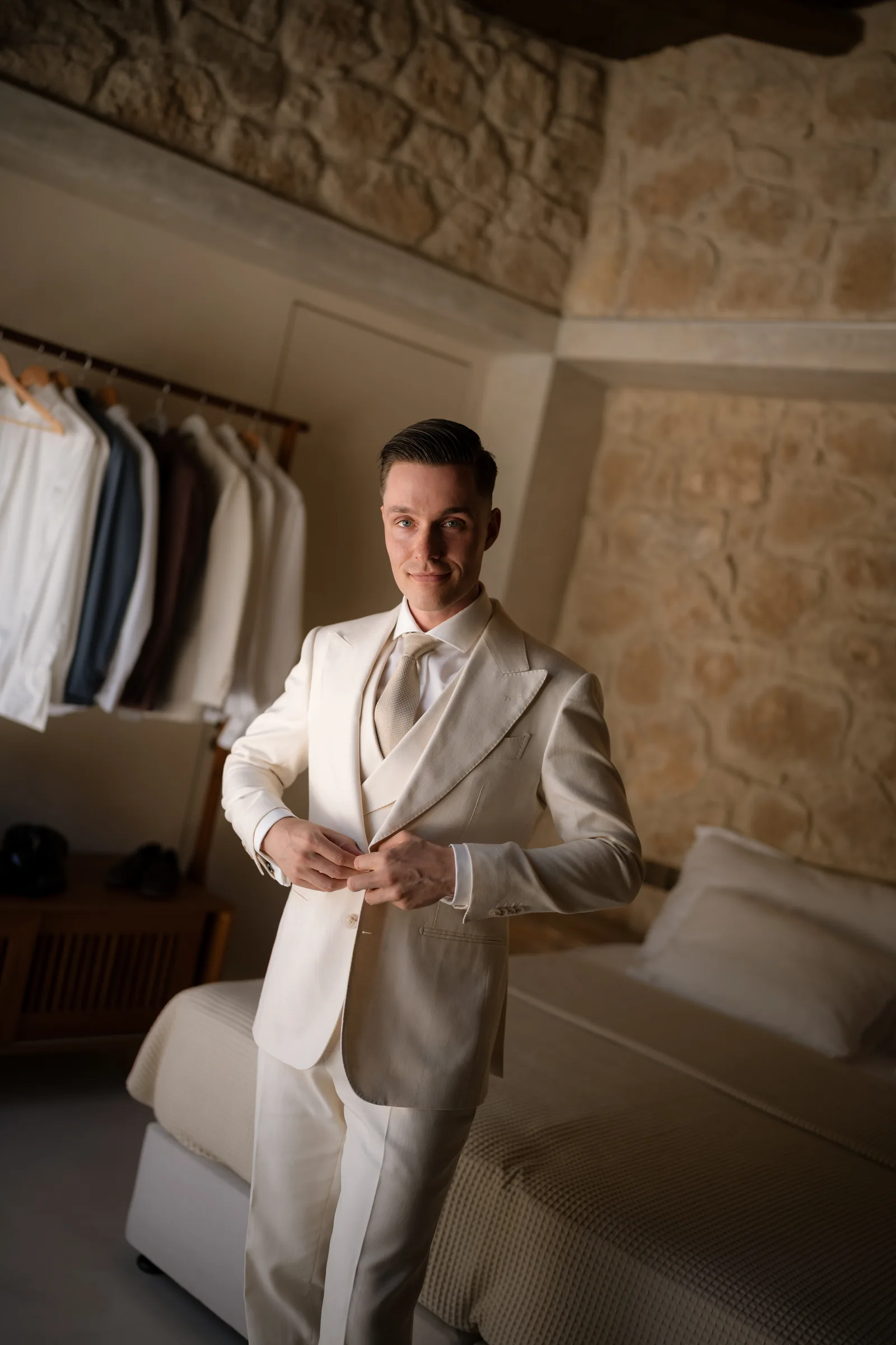Frank buttoning his cream three-piece suit in a stone room during preparations at Liopetro, Kouklia, Paphos, Cyprus.