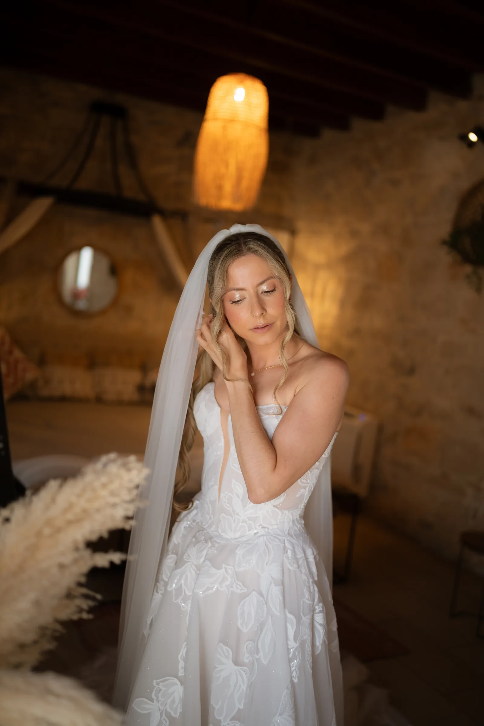Franziska tucking her hair beneath her long veil in the warm boho-styled stone room during preparations at Liopetro, Paphos.