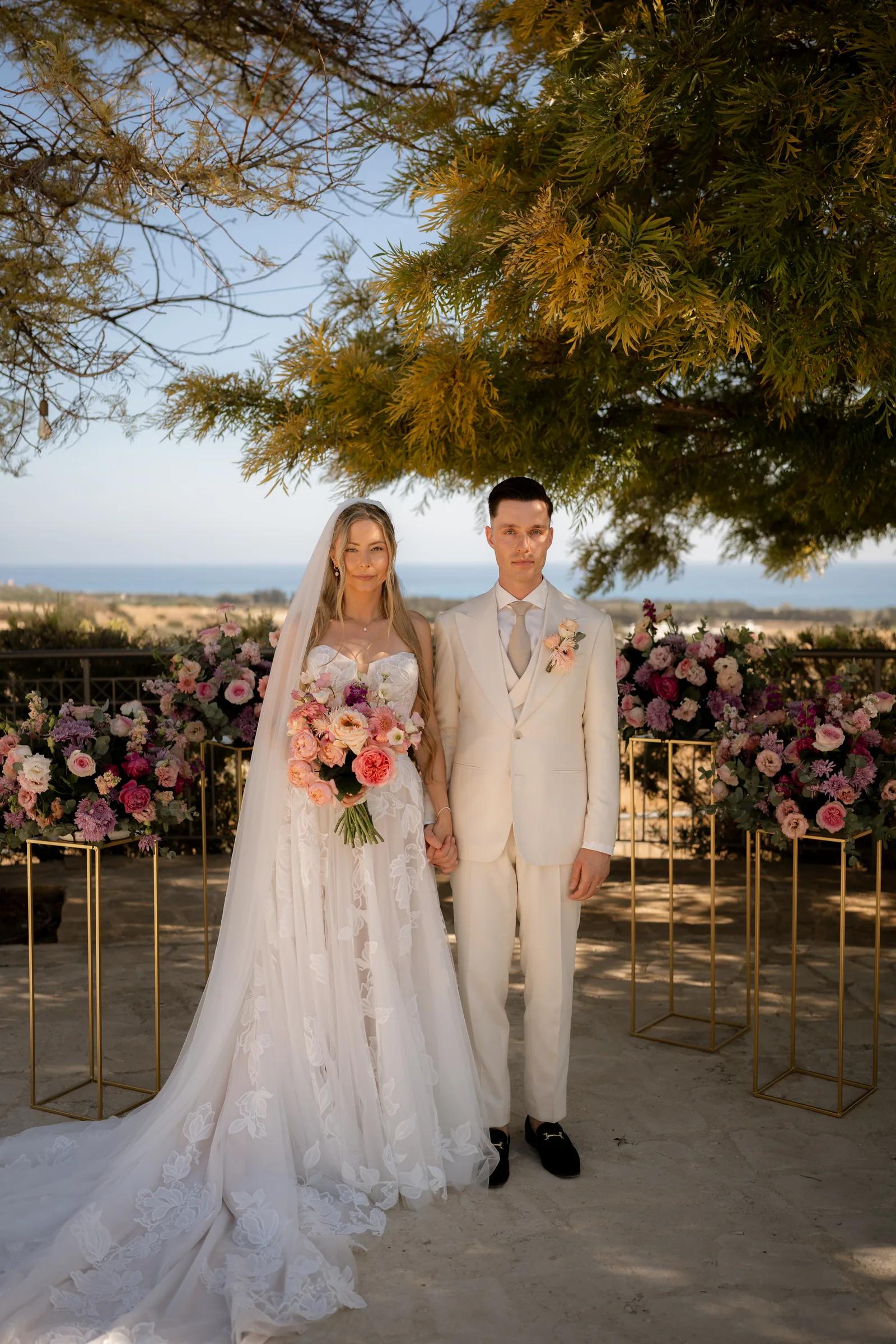 Guests in summer pastels applauding as Frank and Franziska exit their ceremony with bouquet raised at Liopetro, Paphos, Cyprus.