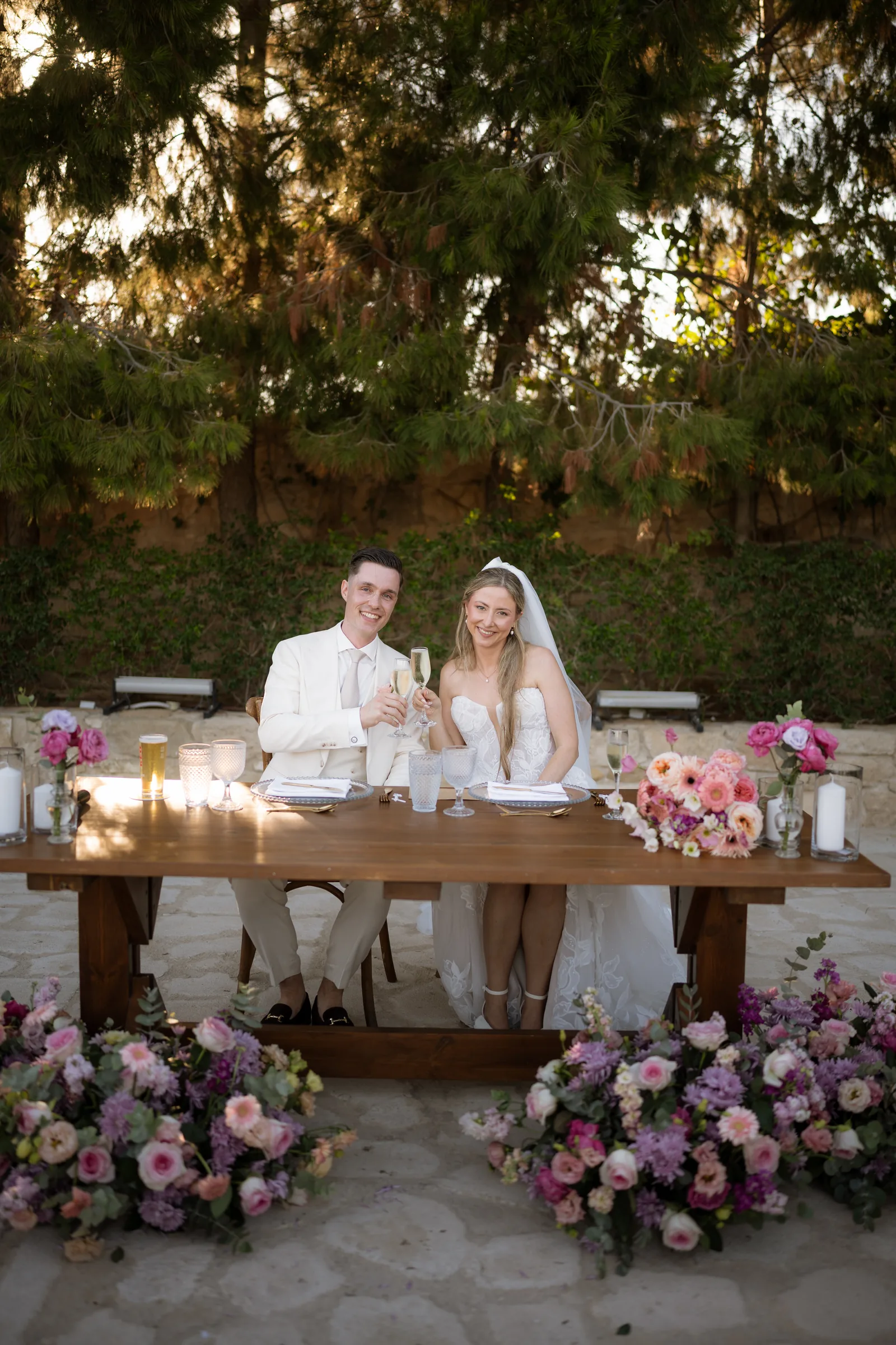 Frank and Franziska toasting at their sweetheart table banked with pink and lilac flowers at Liopetro, Kouklia, Paphos.