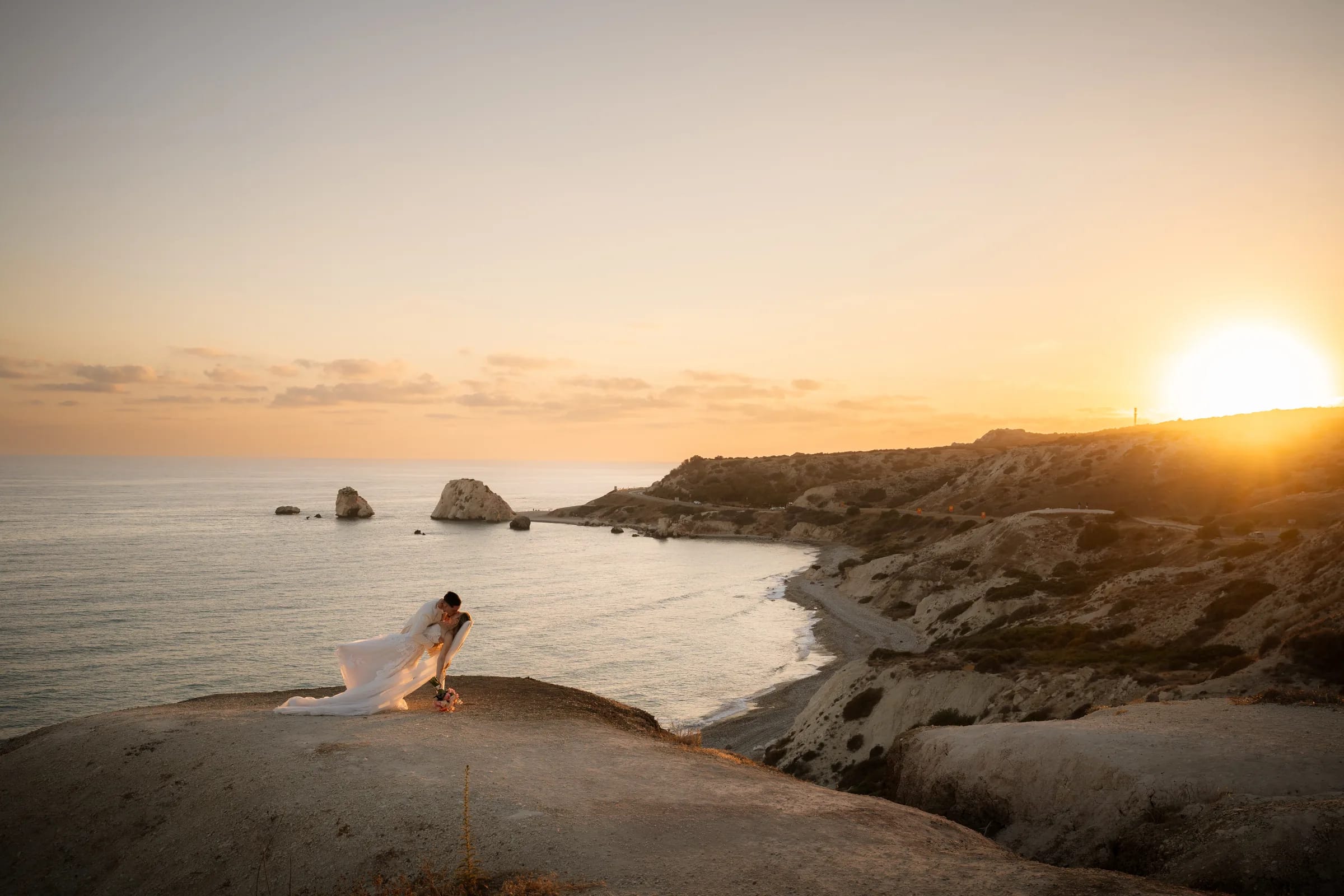 Frank dipping Franziska for a kiss on the clifftop at Aphrodite's Rock as the sun sets over the Paphos coast.