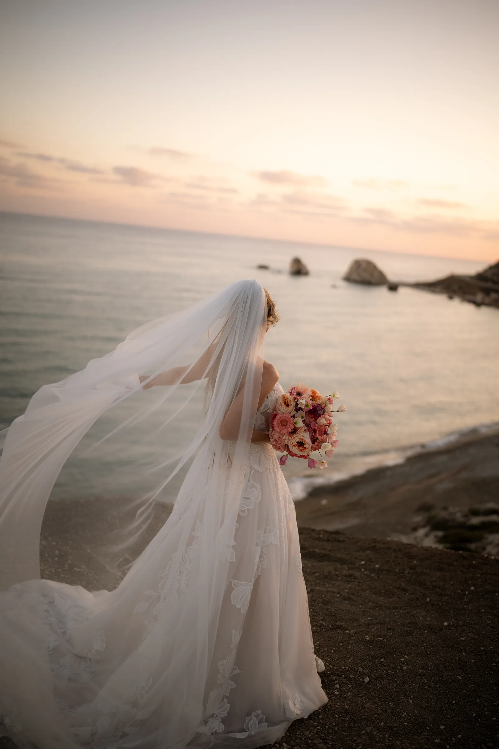 Franziska looking out over the bay at Aphrodite's Rock, her long veil sweeping out on the breeze at sunset, near Paphos, Cyprus.