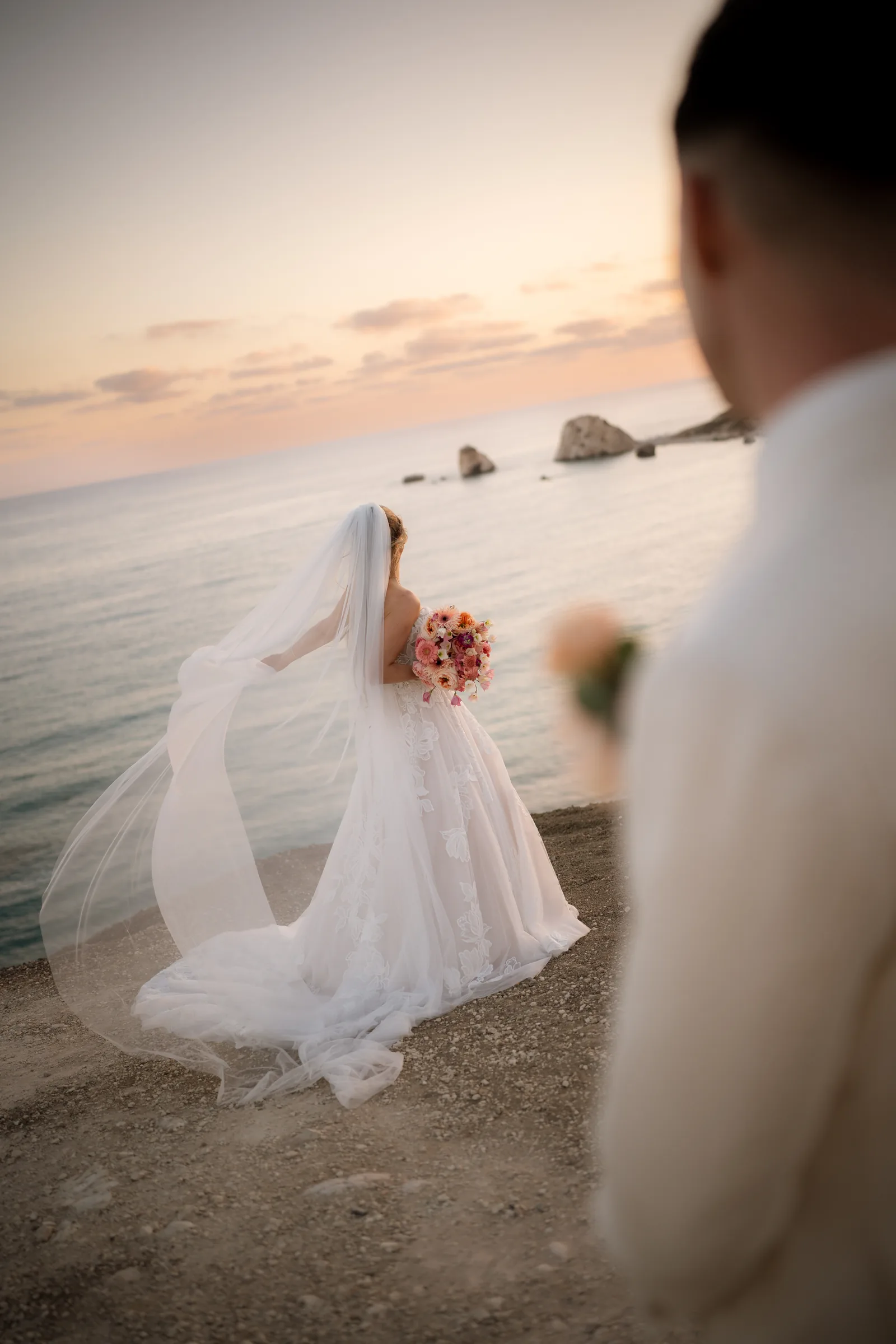 Frank and Franziska touching foreheads beneath her veil in golden light at Aphrodite's Rock, Paphos.