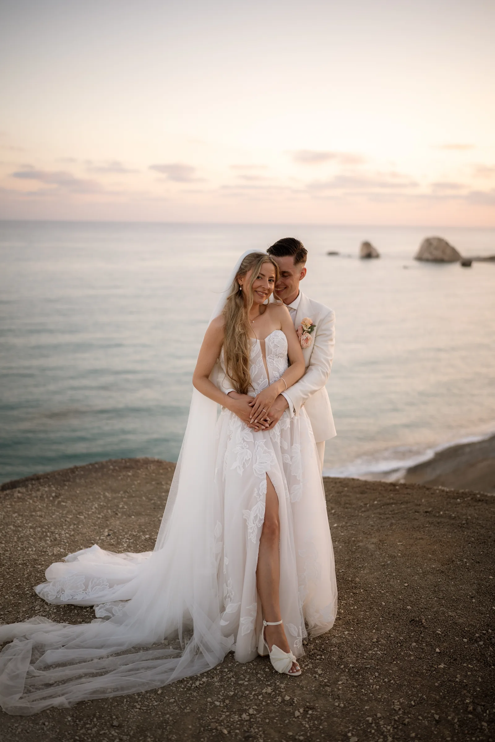 Franziska leaning into Frank in a strapless gown with a leg-split at Aphrodite's Rock at dusk, Paphos.