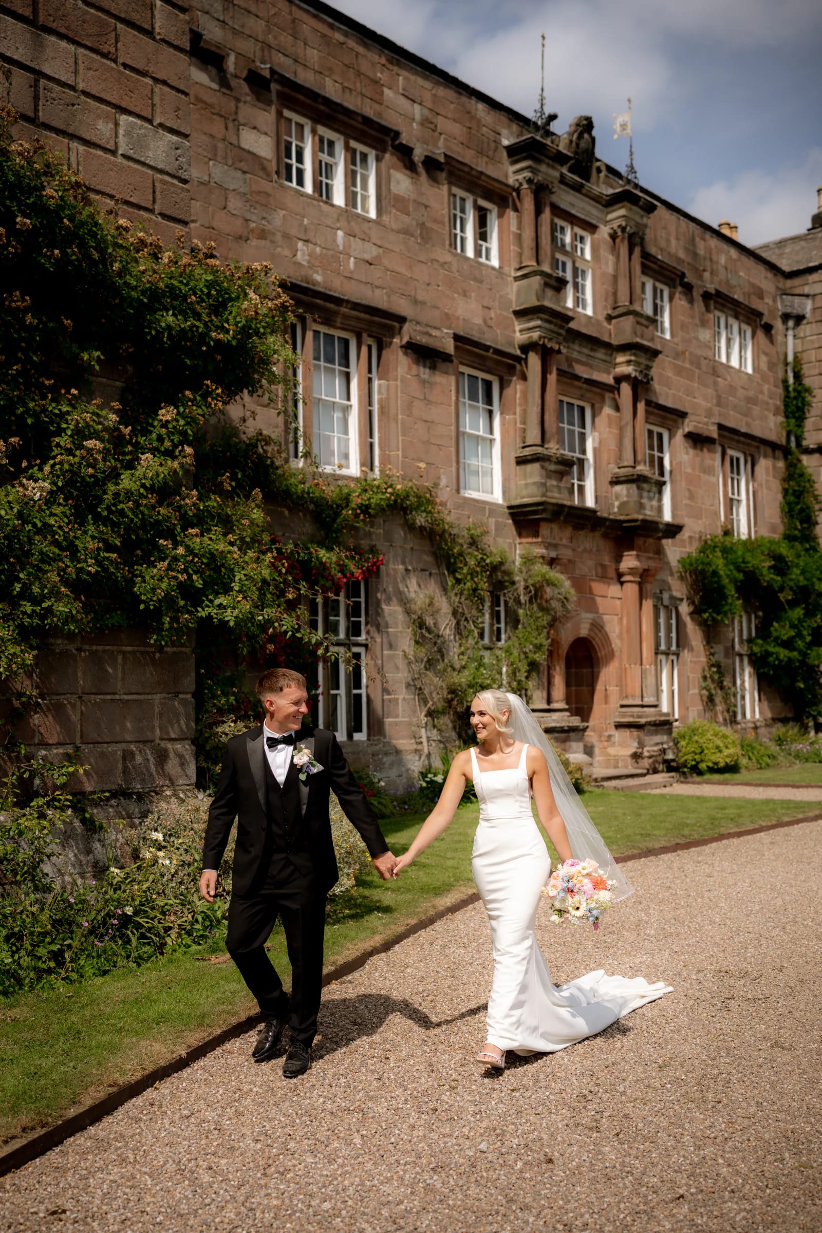Josh and Ellie walking hand in hand in front of Browsholme Hall after their wedding ceremony