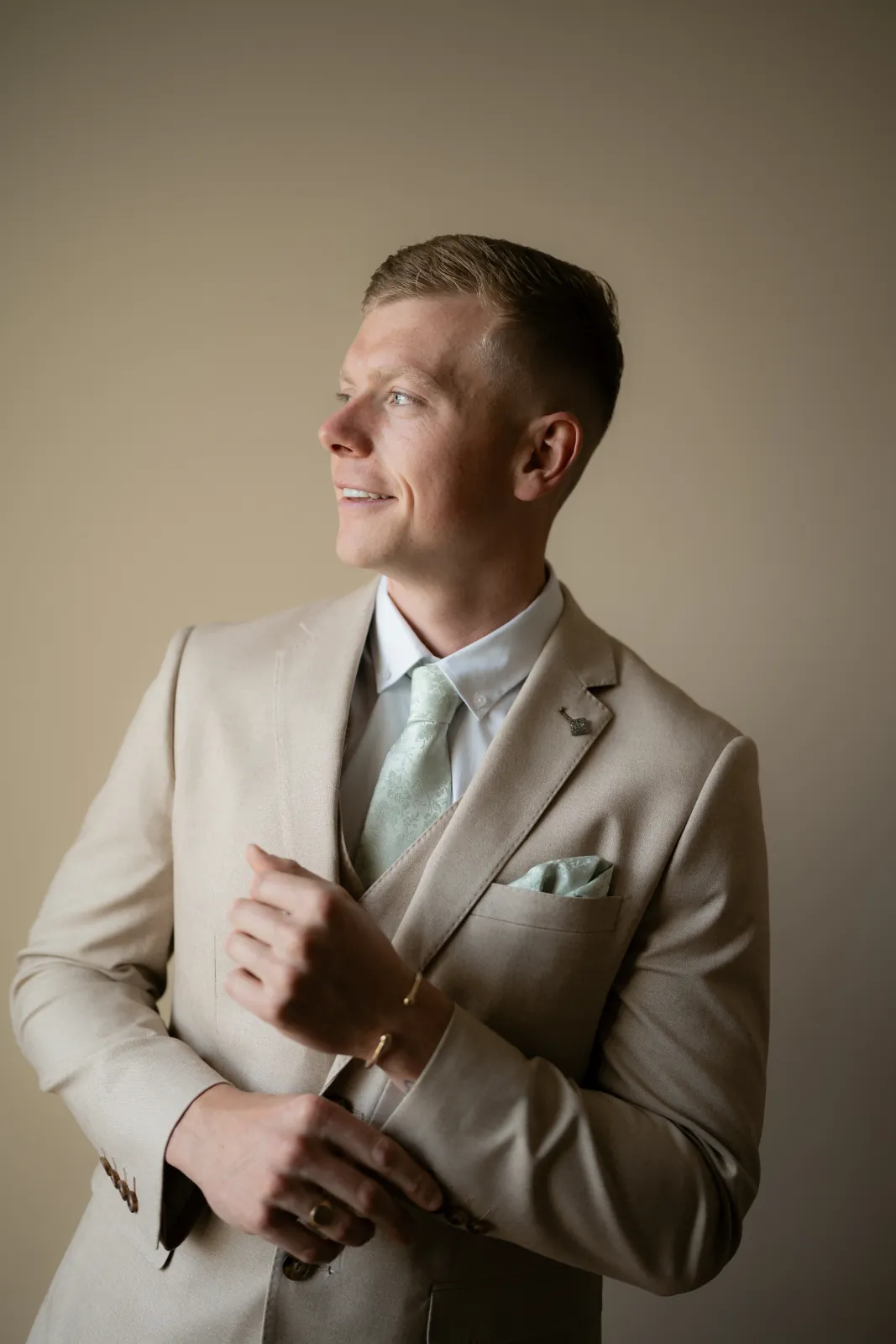 Groom Aaron adjusting his cuff in a sand-coloured suit and sage-green tie during preparations, Paphos, Cyprus.