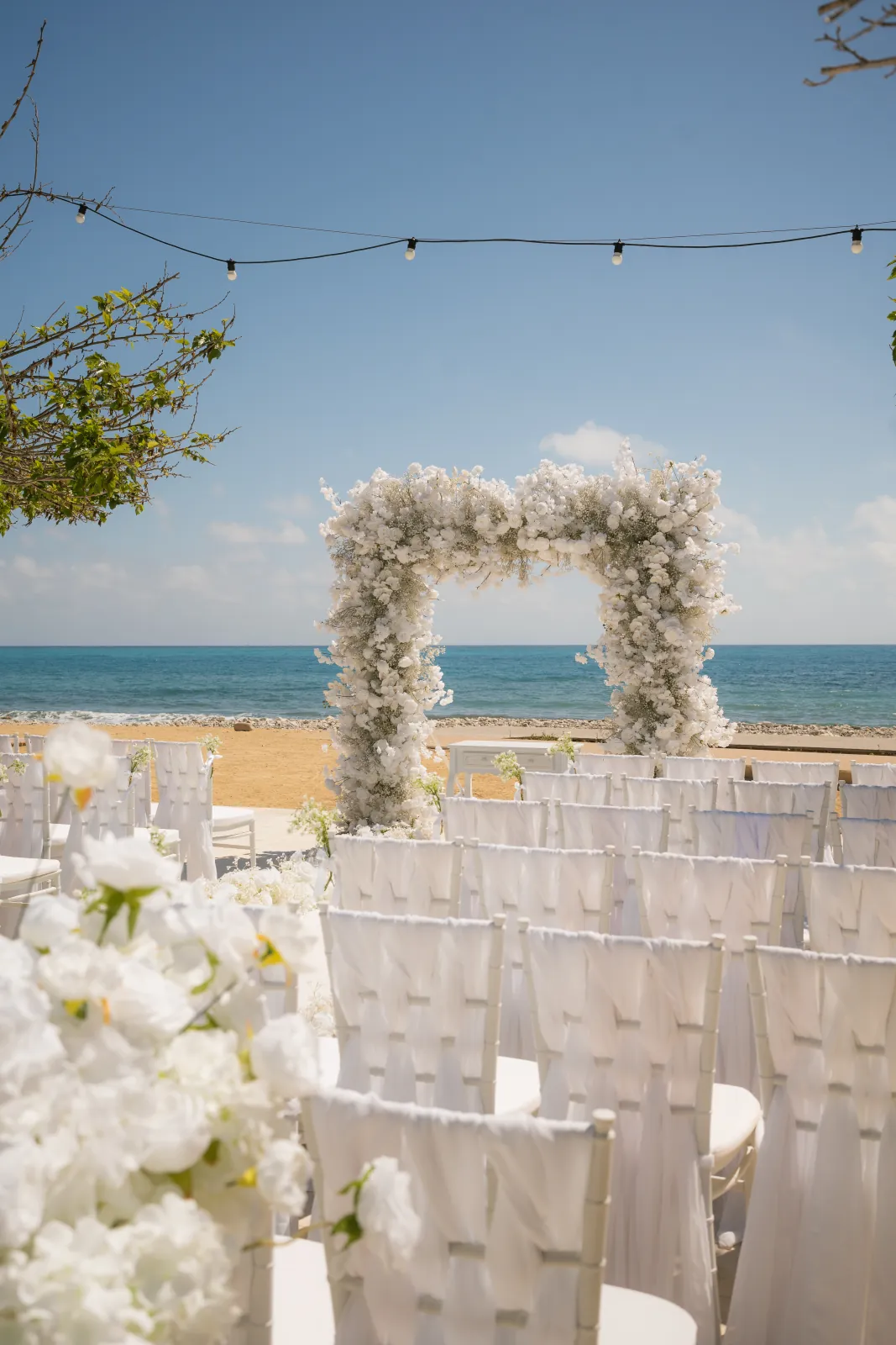 White floral arch and chiffon-draped chairs set on the deck with the sea behind at Coral Residences, Paphos.