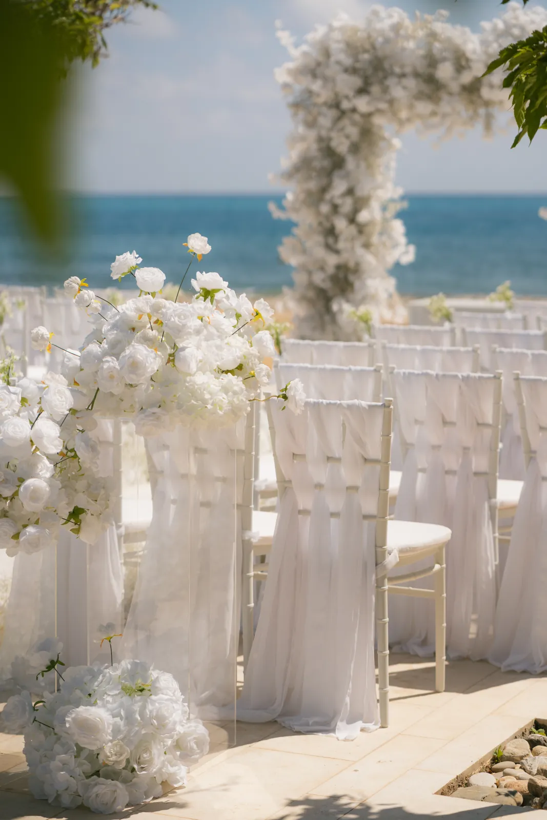 Chiffon-draped chiavari chairs and white aisle florals overlooking the sea at Coral Residences, Paphos.