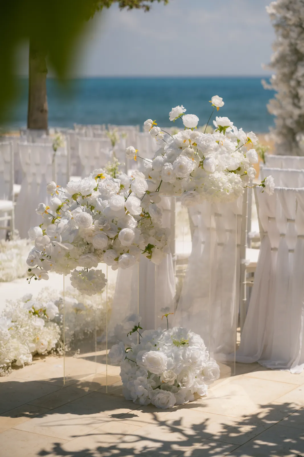 A white floral arrangement on a clear plinth with the sea behind at Coral Residences, Paphos.
